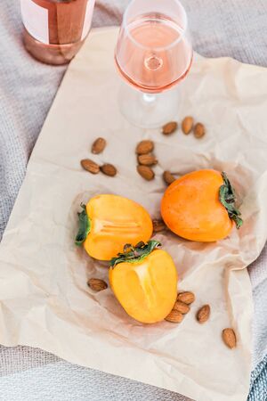 Picnic on the beach with persimmons, almond and bottle of rose wine on beige blanket. Lifestyle view.の写真素材