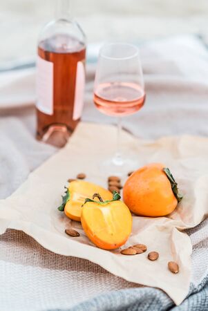 Picnic on the beach with persimmons, almond and bottle of rose wine on beige blanket. Lifestyle view.の写真素材