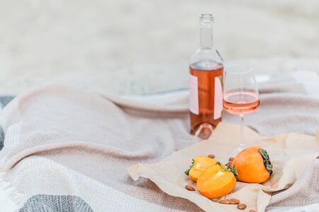 Picnic on the beach with persimmons, almond and bottle of rose wine on beige blanket. Lifestyle view.の写真素材