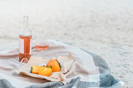 Picnic on the beach with persimmons, almond and bottle of rose wine on beige blanket. Lifestyle view.の写真素材
