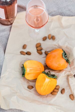 Picnic on the beach with persimmons, almond and bottle of rose wine on beige blanket. Lifestyle view.の写真素材