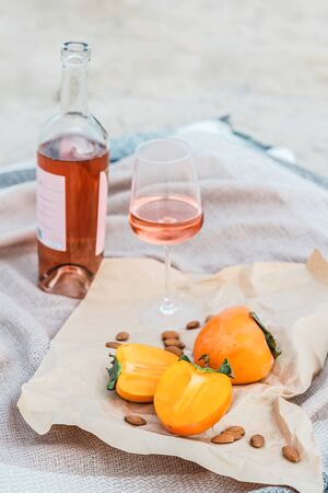 Picnic on the beach with persimmons, almond and bottle of rose wine on beige blanket. Lifestyle view.の写真素材