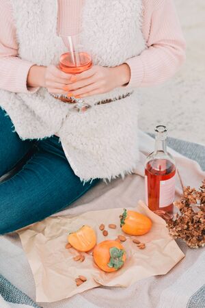 Woman with glass of rose wine is sitting on the beach, having autumn picnic herself. Being outdoors.の写真素材