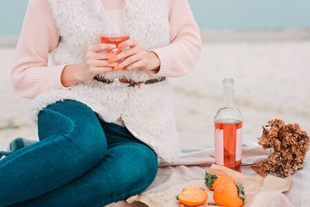 Woman with glass of rose wine is sitting on the beach, having autumn picnic herself. Being outdoors.の写真素材