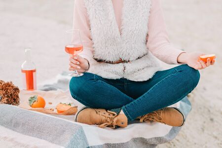 Woman with glass of rose wine is sitting on the beach, having autumn picnic herself. Being outdoors.の写真素材
