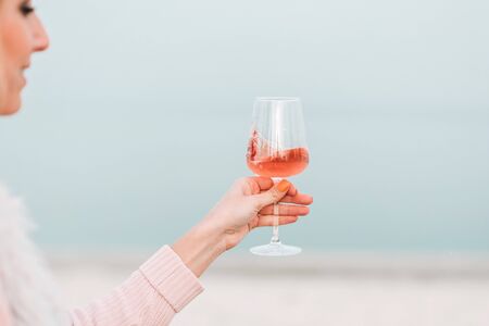 Woman with glass of rose wine is having autumn picnic on the beach. Being outdoors.の写真素材