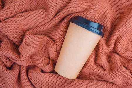 Coffee paper cup on orange knitted blanket background, top view flat lay. Take away coffee cup.の写真素材
