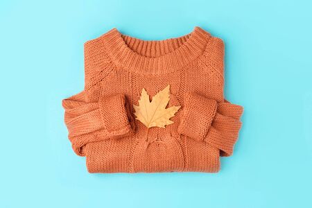 Yellow autumn leaf on orange knitted sweater background, top view flat lay on blue.の写真素材