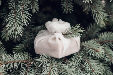 Christmas present wrapped with white furoshiki fabric on fir branches. Eco friendly gift, zero waste concept.の写真素材