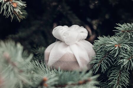 Christmas present wrapped with white furoshiki fabric on fir branches. Eco friendly gift, zero waste concept.の写真素材