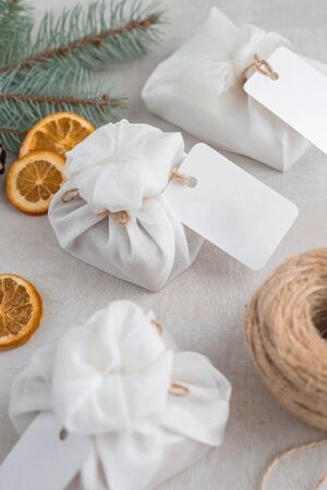 Christmas presents wrapped with white furoshiki fabric, labels and dried orange slices. Eco friendly gift, zero waste concept.の写真素材