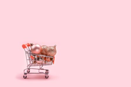 Christmas tree decorations and balls in miniature shopping cart with on pastel pink background with copy space. Christmas shopping concept.の写真素材