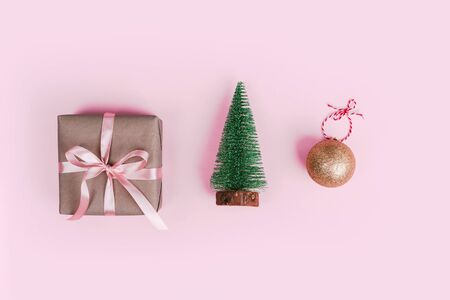Miniature christmas tree, gift wrapped in craft paper and christmas tree ball decoration on pale pink background. Flat lay with copy space. Holiday concept.の写真素材