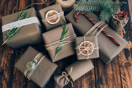 Presents and gifts wrapped in craft paper with decoration on brown wooden background. Flat lay, close up. Holiday zero waste concept.の写真素材