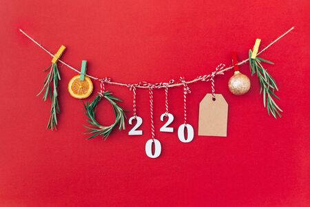 Christmas handmade garland made of 2020 wooden numerals and fir tree branches and other christmas decorations on red background. Christmas, New Year, zero waste concept.の写真素材