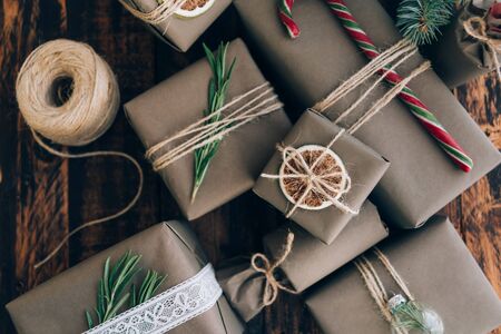 Presents and gifts wrapped in craft paper with decoration on brown wooden background. Flat lay, close up. Holiday zero waste concept.の写真素材