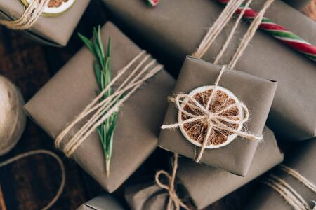 Presents and gifts wrapped in craft paper with decoration on brown wooden background. Flat lay, close up. Holiday zero waste concept.の写真素材