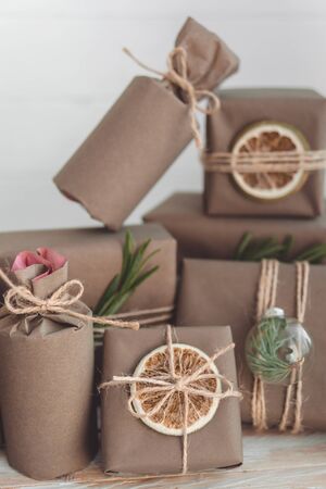 Pile of presents and gifts wrapped in craft paper with decoration on white wooden background. Flat lay, close up. Holiday zero waste concept.の写真素材