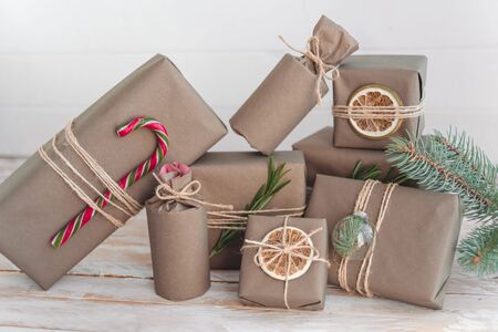 Pile of presents and gifts wrapped in craft paper with decoration on white wooden background. Flat lay, close up. Holiday zero waste concept.の写真素材