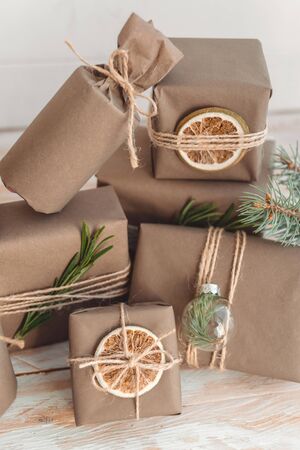 Pile of presents and gifts wrapped in craft paper with decoration on white wooden background. Flat lay, close up. Holiday zero waste concept.の写真素材