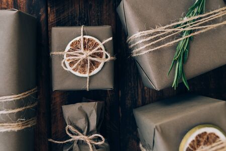 Presents and gifts wrapped in craft paper with decoration on brown wooden background. Flat lay, close up. Holiday zero waste concept.の写真素材