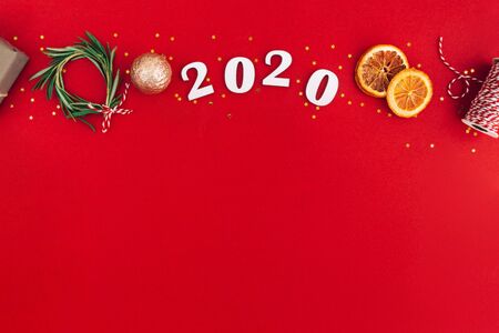 Christmas handmade oval frame made of 2020 wooden numerals and fir tree branches and other christmas decorations on red background. Christmas, New Year, zero waste concept.の写真素材