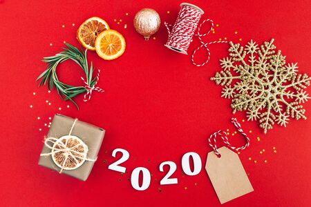 Christmas handmade oval frame made of 2020 wooden numerals and fir tree branches and other christmas decorations on red background. Christmas, New Year, zero waste concept.の写真素材