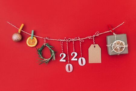 Christmas handmade garland made of 2020 wooden numerals and fir tree branches and other christmas decorations on red background. Christmas, New Year, zero waste concept.の写真素材
