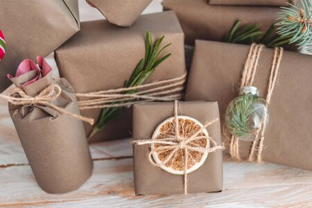 Pile of presents and gifts wrapped in craft paper with decoration on white wooden background. Flat lay, close up. Holiday zero waste concept.の写真素材