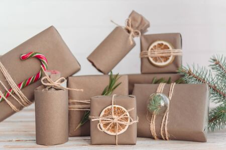 Pile of presents and gifts wrapped in craft paper with decoration on white wooden background. Flat lay, close up. Holiday zero waste concept.の写真素材