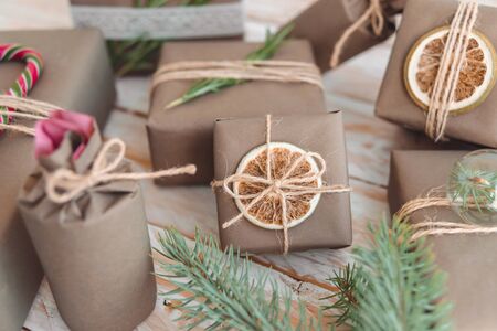 Pile of presents and gifts wrapped in craft paper with decoration on white wooden background. Flat lay, close up. Holiday zero waste concept.の写真素材