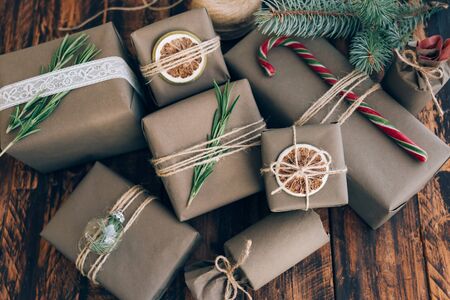 Presents and gifts wrapped in craft paper with decoration on brown wooden background. Flat lay, close up. Holiday zero waste concept.の写真素材