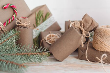 Pile of presents and gifts wrapped in craft paper with decoration on white wooden background. Flat lay, close up. Holiday zero waste concept.の写真素材