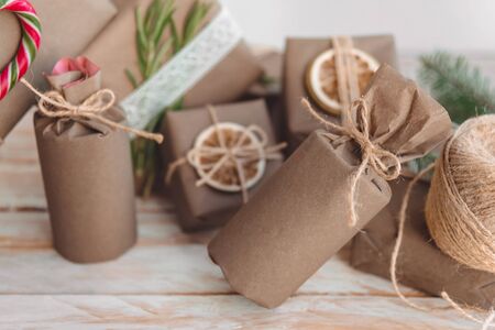 Pile of presents and gifts wrapped in craft paper with decoration on white wooden background. Flat lay, close up. Holiday zero waste concept.の写真素材