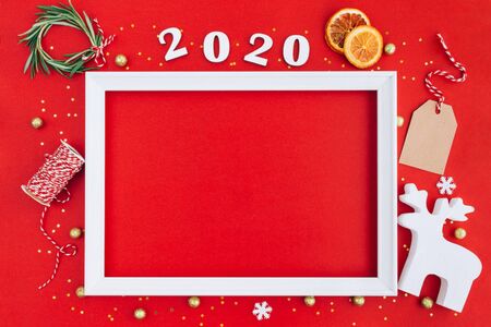 Festive christmas white frame made of christmas decorations and 2020 wooden numerals on red background with copy space. Flat lay, top view. Christmas, winter, New Year concept.の写真素材