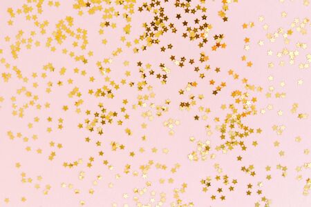 Golden star glitter confetti on pale pink background. Festive holiday background. Celebration concept. Top view, flat lay.の写真素材