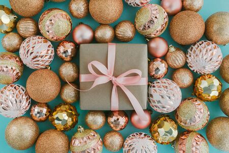 Gift box wrapped in craft paper with pink ribbon and golden Christmas tree balls on pale blue background with glitters. Festive concept, top view.の写真素材