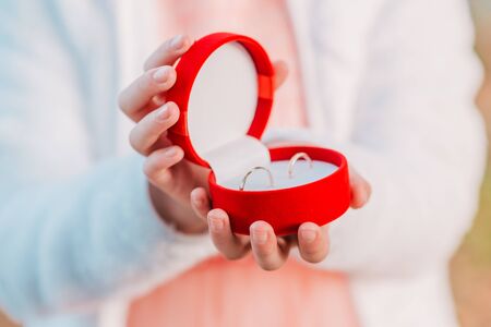 Red gift box with wedding rings in kids hands. Cute moment, close up.の写真素材