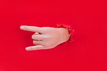 Male hand shows a rock and roll sign through a hole in red background.の写真素材