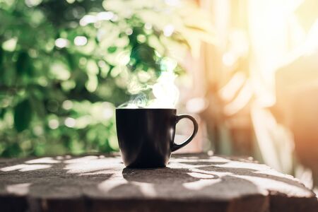 Black big cup of black tea with white steam on stone balcony edge in morning light with copy space.の写真素材