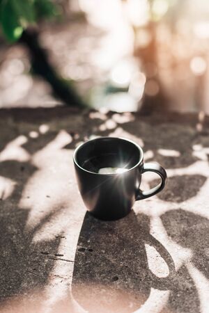 Black big cup of black tea with white steam on stone balcony edge in morning light with copy space.の写真素材