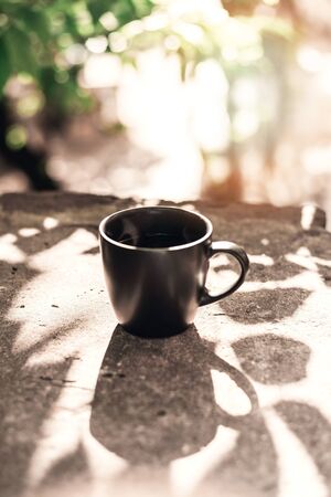 Black big cup of black tea with white steam on stone balcony edge in morning light with copy space.の写真素材