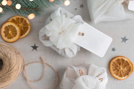 Christmas presents wrapped with white furoshiki fabric, labels and dried orange slices. Eco friendly gift, zero waste concept.の写真素材