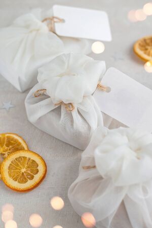 Christmas presents wrapped with white furoshiki fabric, labels and dried orange slices. Eco friendly gift, zero waste concept.の写真素材