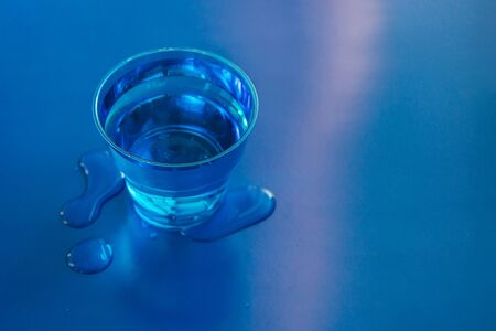 Filled blue glass of water on blue neon background with spilled water on it. Copy space.の写真素材