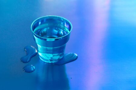 Filled blue glass of water on blue neon background with spilled water on it. Copy space.の写真素材