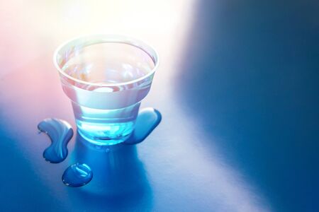 Filled blue glass of water on blue neon background with spilled water on it. Copy space.の写真素材