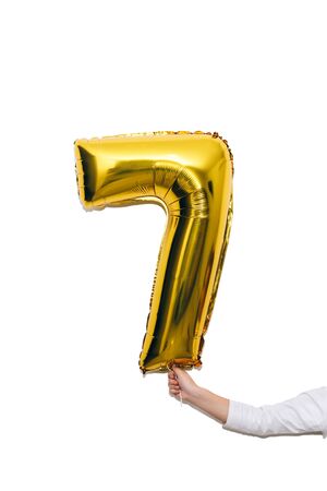 Kid's hand with golden balloon number seven, 7 isolated on white background. Birthday concept.の写真素材