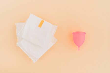 Feminine hygiene products - menstrual cup and stack of sanitary pads on pale orange background. Top view.の写真素材