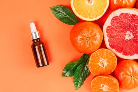 Fresh ripe mandarins, grapefruit and oranges with green leaves and glass bottle with essential oil on orange background. Top view.の写真素材